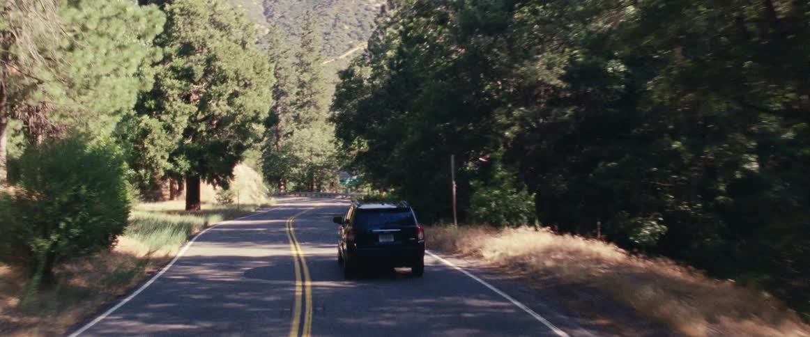 Black vehicle drives on a winding country road