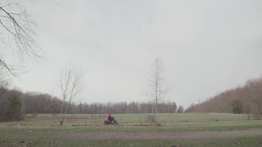A person riding a small tractor across a path on a grass plain in a park