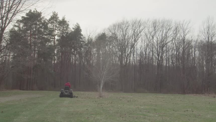 Man cutting grass in a field with trees in the background