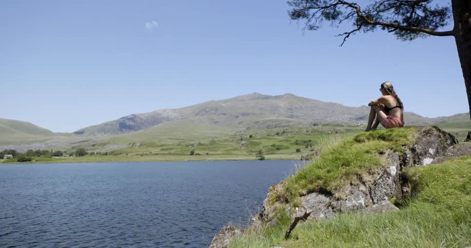 Woman sitting on a grassy hill overlooking the lake and mountains