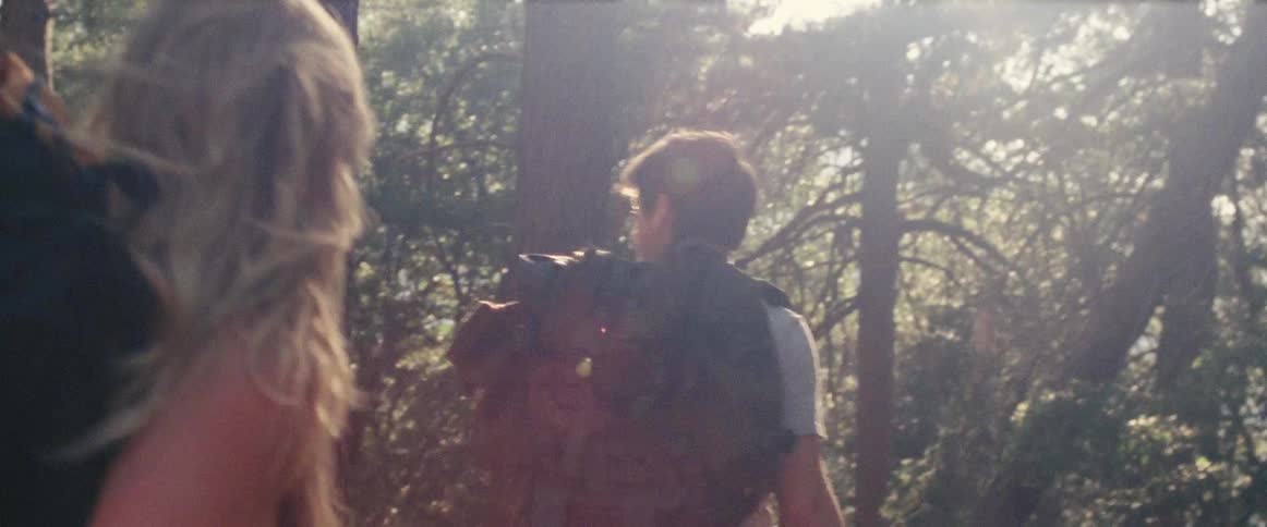 A man and a woman with  backpacks walking through the woods