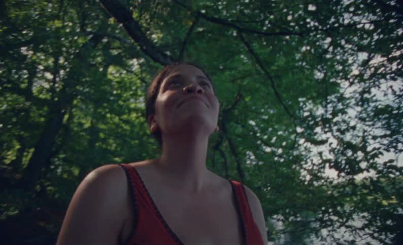 The woman is standing by the lake looking up at tree branches