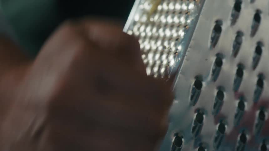 Close up of a person using a steel kitchen grater to shred a vegetable while preparing food