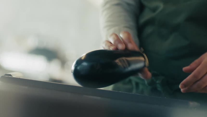 A person is holding a brinjal and get ready to slice it