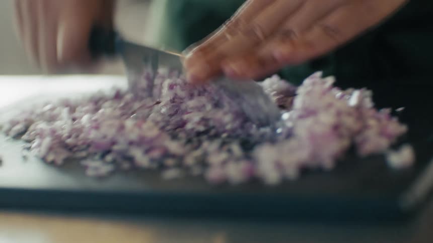 Chef rapidly dicing purple onions on a cutting board