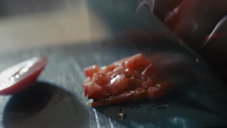 The video shows a closeup of a person dicing red tomatoes on a black cutting board with a knife the action is fastpaced and the knife flashes as it chops the vegetables