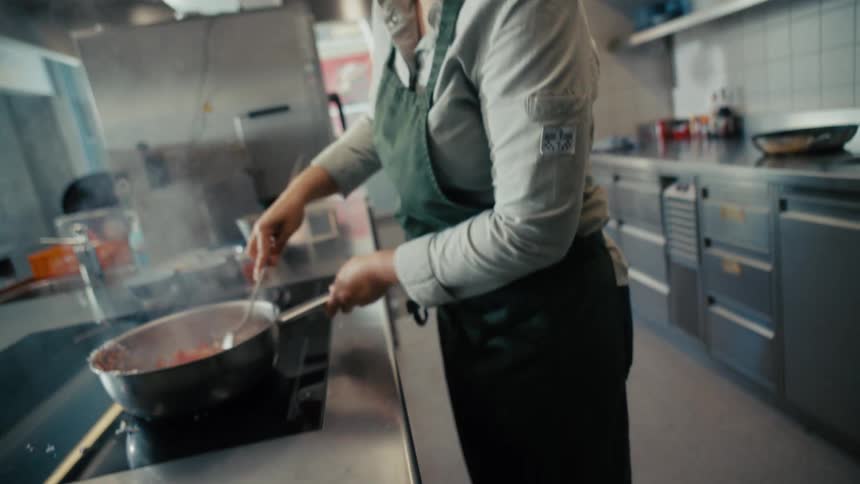 The woman is stirring food in the pan while smiling