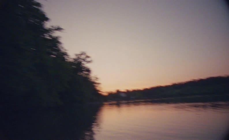 Canoe riding on a lake lined on one side by trees at sunset