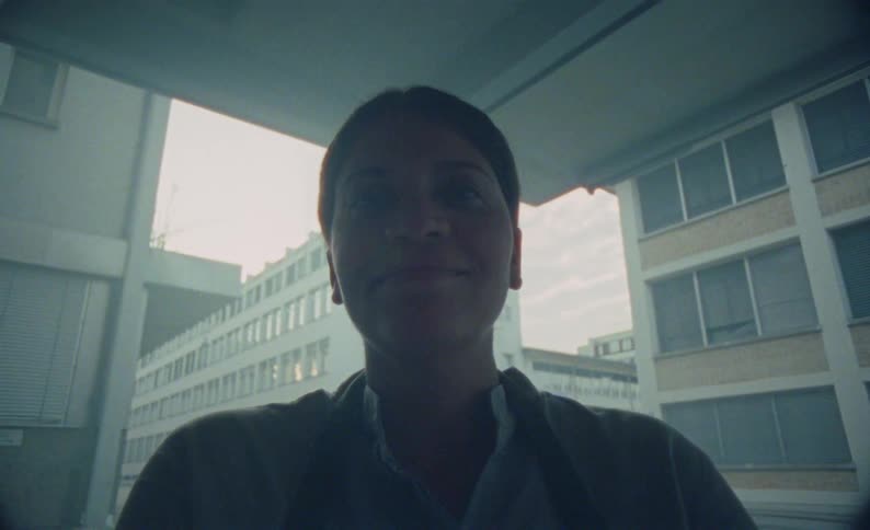 A smiling woman filming herself on a city buildings corner balcony