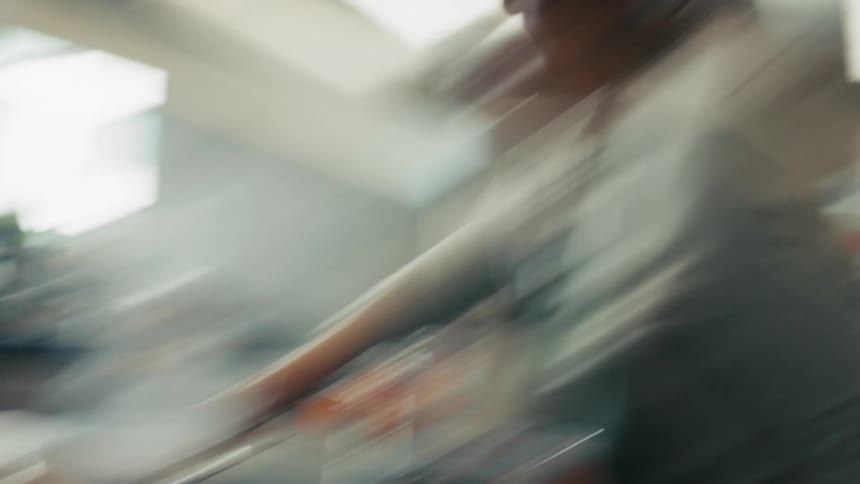 A woman in a large kitchen moves frantically while cooking to use a spatula to stir a pot