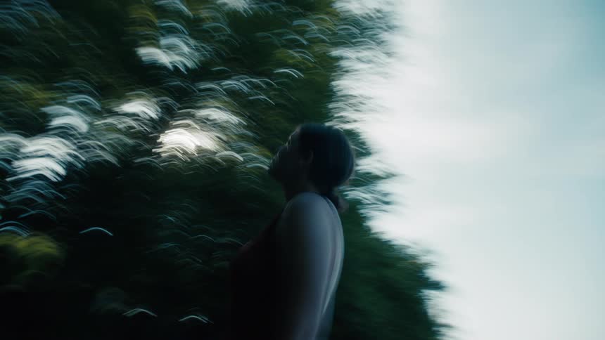 The video shows a lowangle shot of a person jogging or running outdoors with the camera angled up toward the sky the sunlight flares through the leaves of the trees creating a dynamic lensflaring effect the person is silhouetted against the bright
