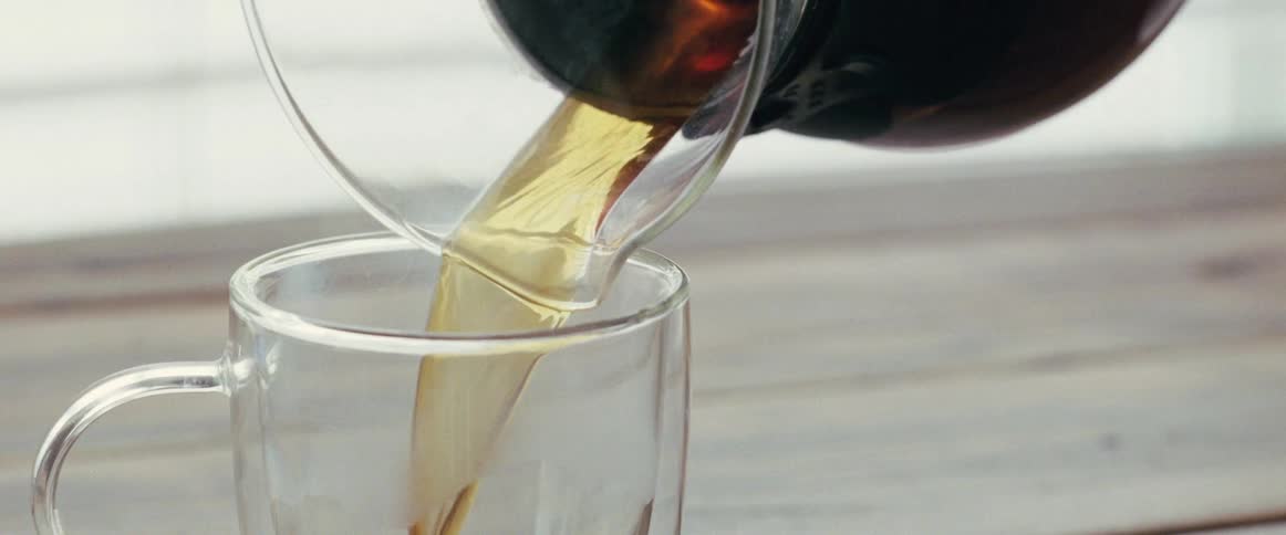 A close up view of a coffee cup and someone pouring coffee in it