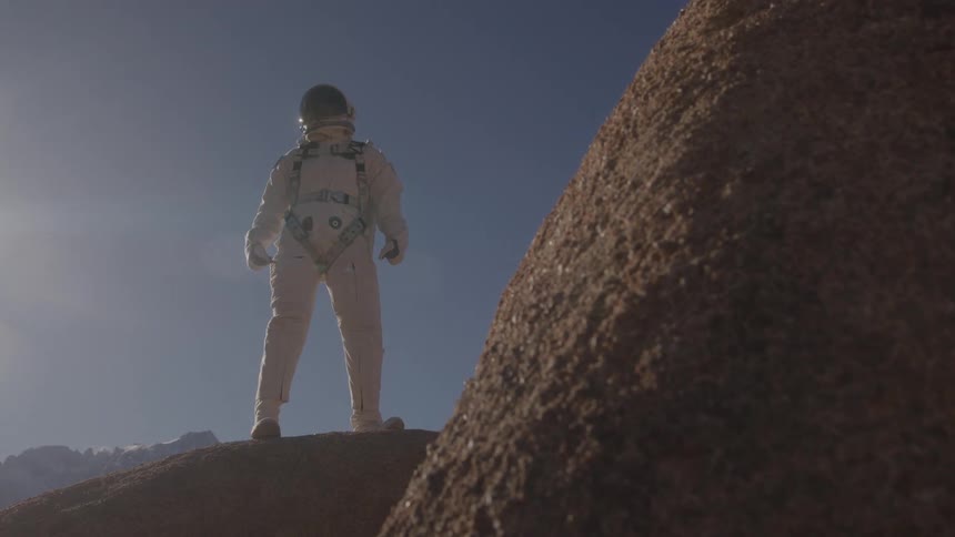 Astronaut in a spacesuit observes the rocky landscape under the sun