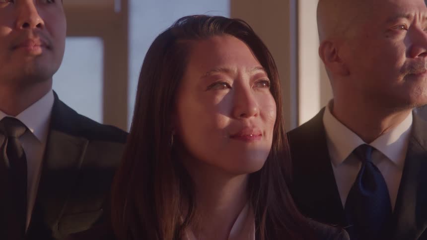 Young asian woman wearing a suit standing between two men in suits outdoors on a sunny day