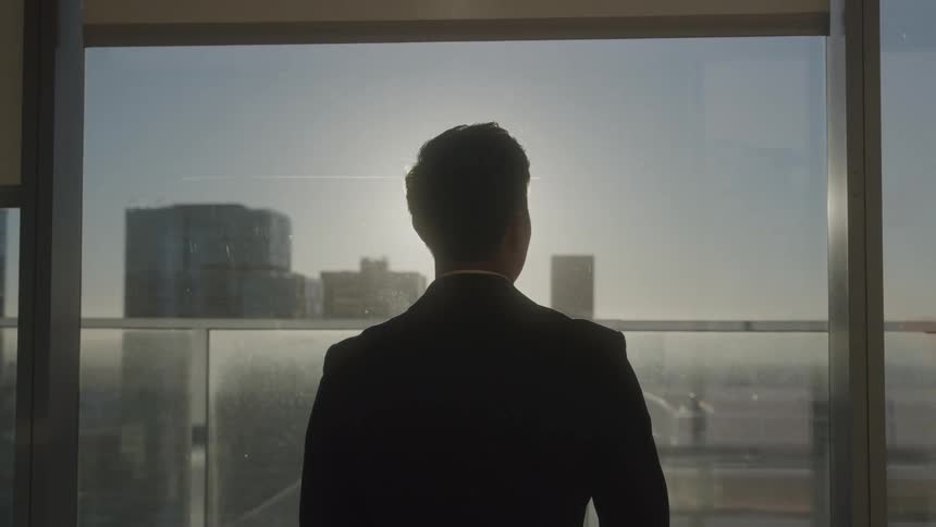 The man looks out the office window at the sunny sky