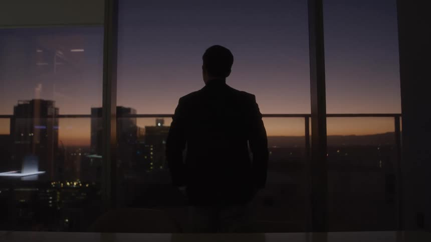 A man in a suit is looking to the sky in a office at sunset