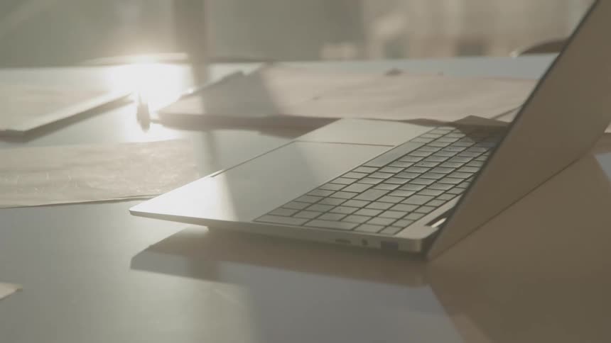 Laptop computer on an office desk surrounded by documents at midday