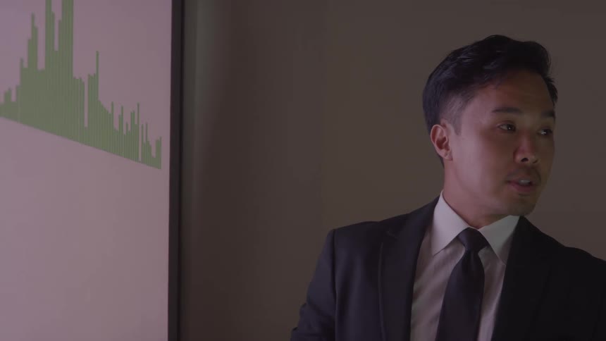 The man is talking and pointing to a graph on the display in the office