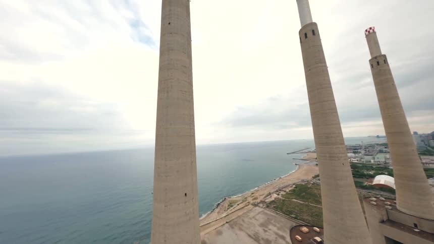 Power plant with a series of chimneys by the shoreline at midday with the cityscape visible in the background