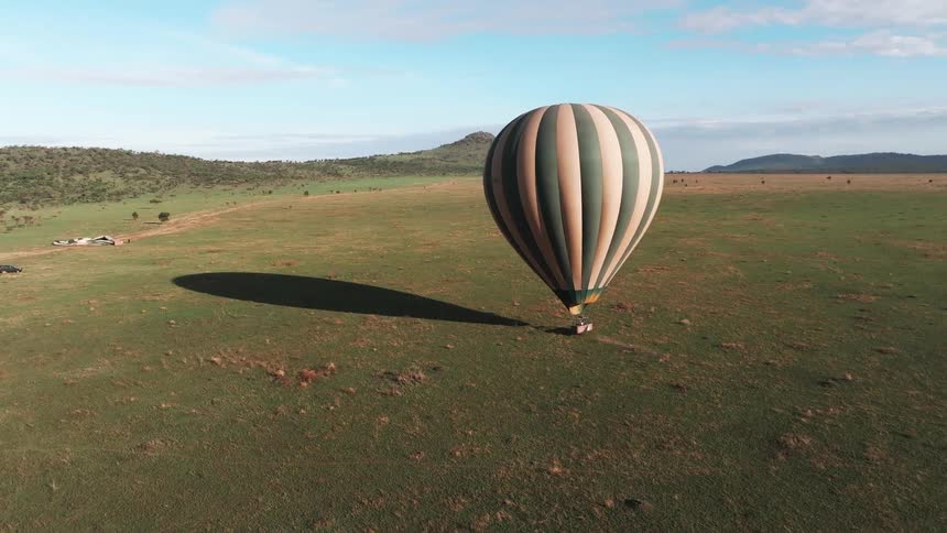 A hot air balloon flies low over land with mountains in the distance