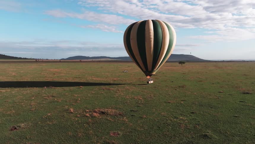 A hot air balloon flies low over land with mountains in the distance