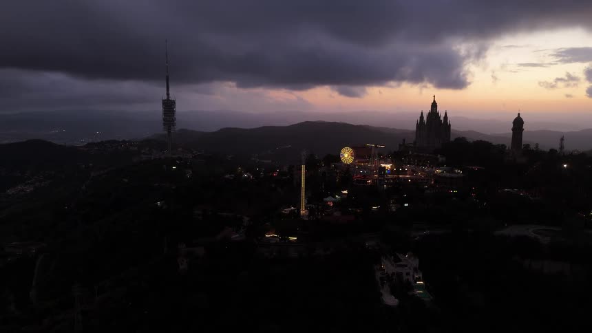 Historic buildings and a resort stand on a hill overlooking a foggy urban valley under a cloudy red tinted sky