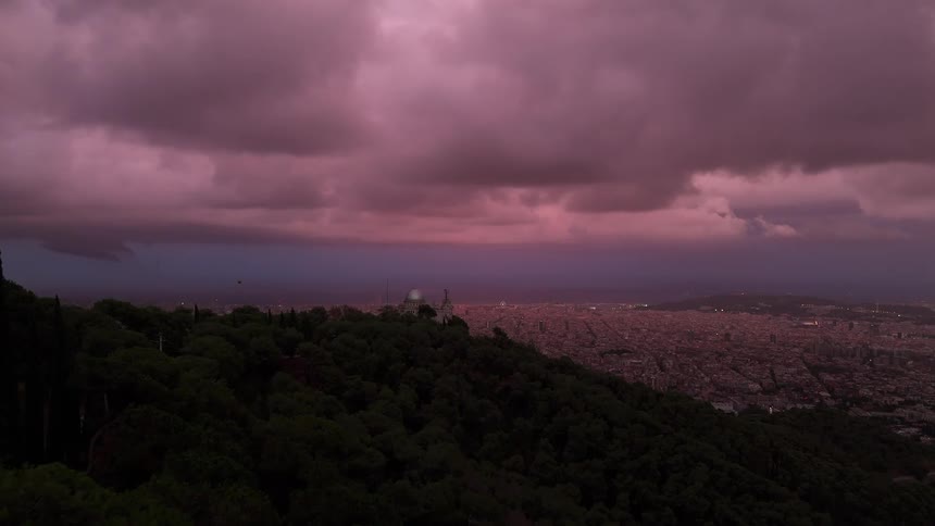 Treecovered hill overlooking a city at sunset with a pink sky