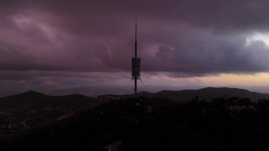 Antenna stands on a hill overlooking an urban valley under a red tinted cloudy sky