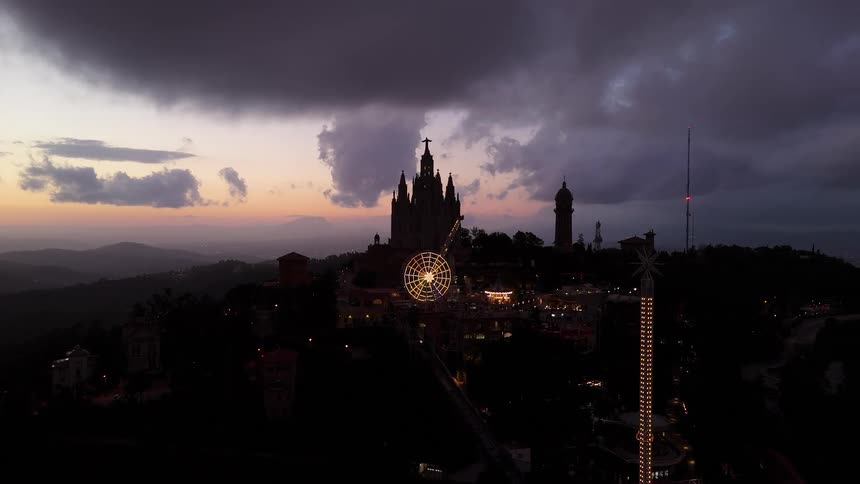 Church illuminated in the background with a ferris wheel and light tower at sunset