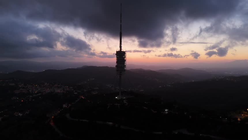 Telecommunications tower lit up at sunset among mountains