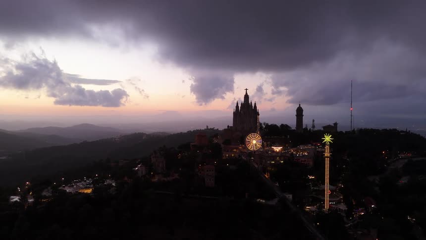 Illuminated castle at dusk with a ferris wheel and mountains in the background