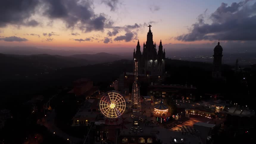 Ferris wheel lit up in front of a church on the hill at sunset