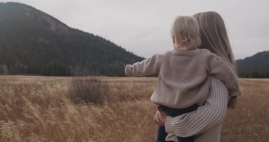 Mother carries her daughter in her arms while looking at the field landscape