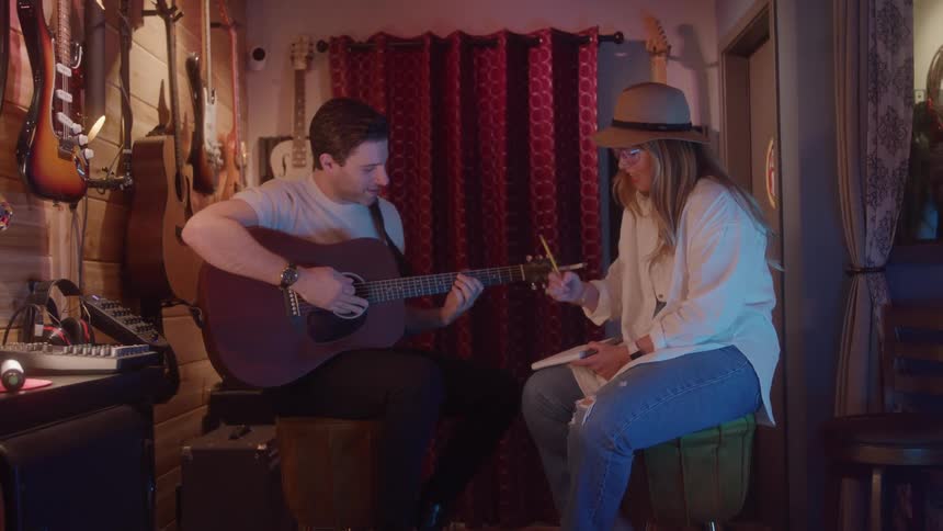 A man and woman are writing songs while the man plays guitar