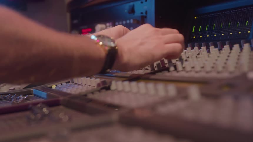 A hand tweaks the faders on a mixing console conveying focused technical concentration