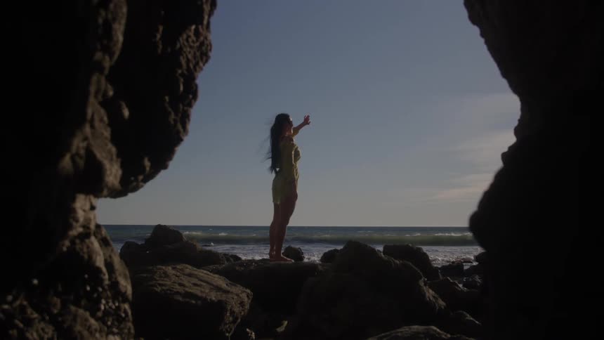 Woman on top of a rock at the edge of a beach