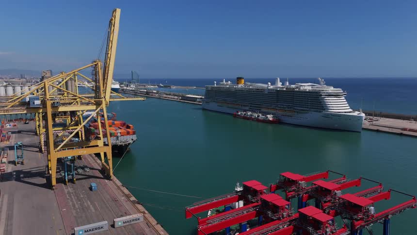 An aerial view framed by blue gantries showing a busy harbor of cranes container stacks and a large cruise ship moored at the pier