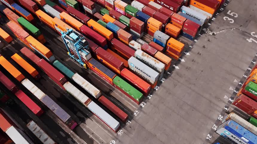 A yard with shipping containers with a vehicle moving through the rows of containers