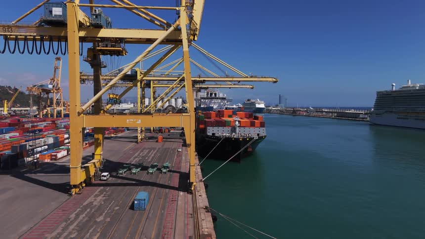 Container ship loaded with shipping containers sits near the loading cranes at the loading dock during the daytime