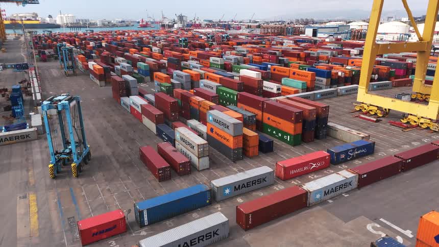 A yard with shipping containers and a vehicle moving through the rows of containers