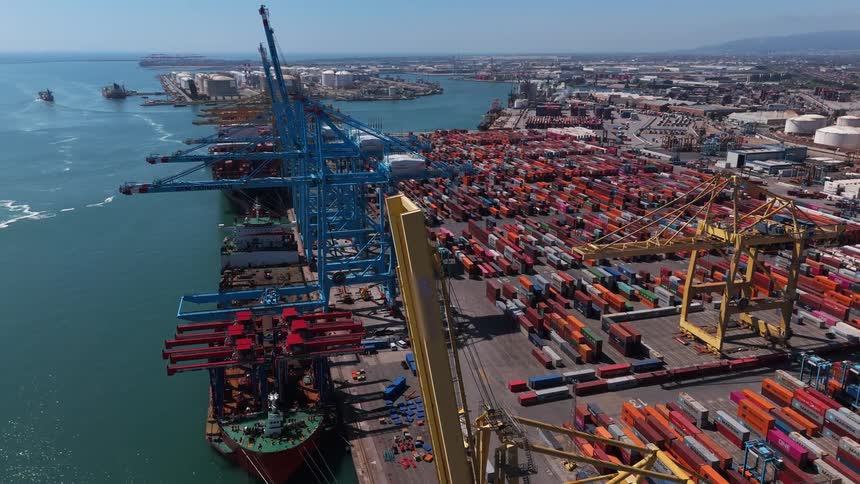 Based on the video a large cargo ship is docked in a port it is surrounded by large cranes and thousands of brightly colored shipping containers which are stacked high in the port