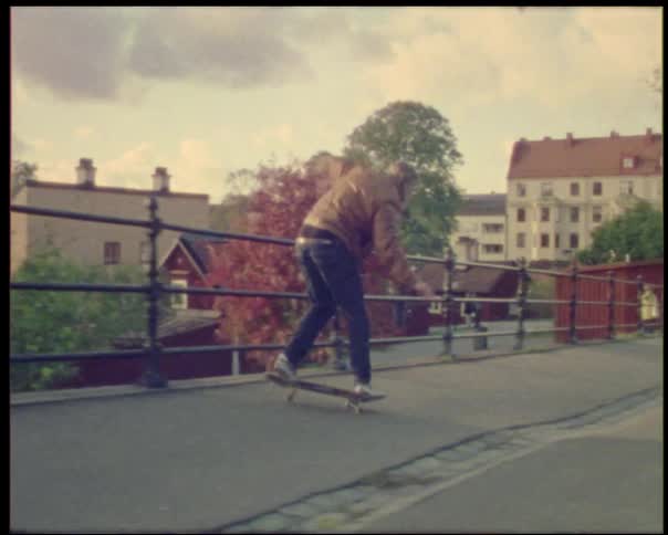 Young man on a skateboard jumping onto a railing and back to the road wearing a hoodie and jeans in the city at midday