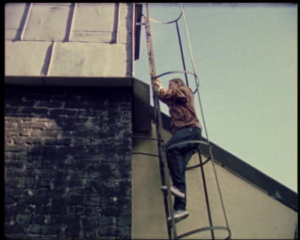 A man in a brown jacket and jeans is climbing a vertical ladder on the side of a building he is nearing the top of the ladder which leads to the roof