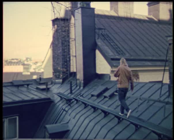 A person walks carefully along a sloped rooftop rail looking focused and steady