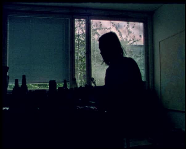 A silhouette of a person with long hair is working at a desk in front of a window the room is dark and the persons shape is only visible due to the light coming from the window