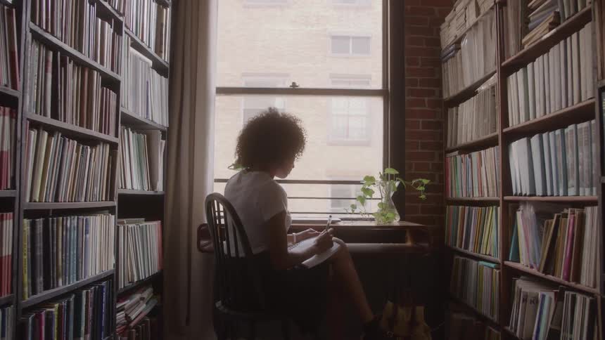 Woman writing in a notebook between bookshelves