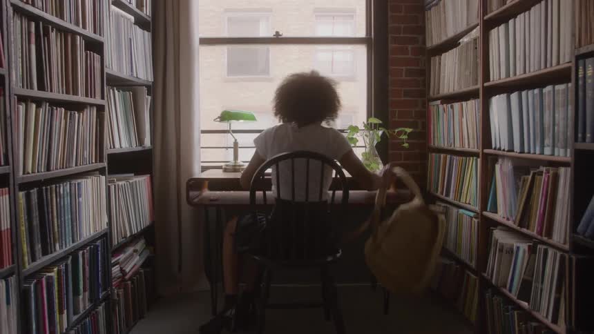 Woman walking through a library corridor towards a bright window