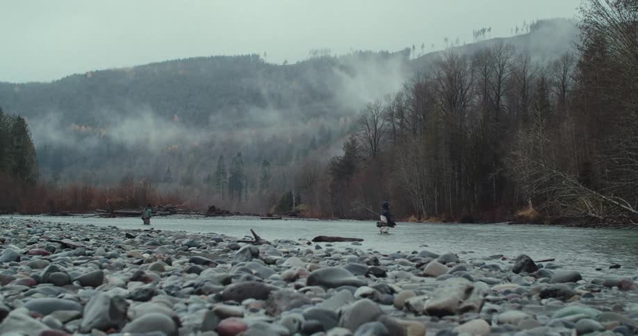 Men fishing in a river surrounded by mountains and mistcovered trees