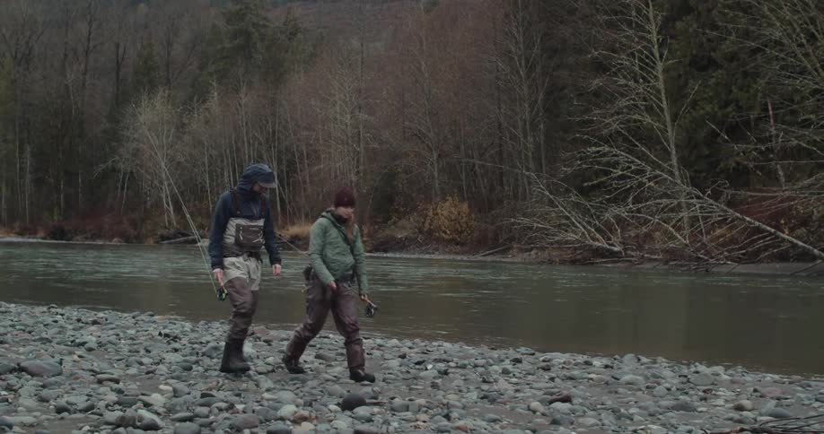 Two anglers walking along a rocky riverbank