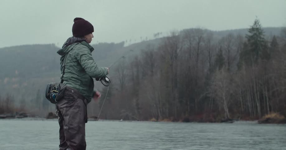 Woman fishing in a river with mountains in the background